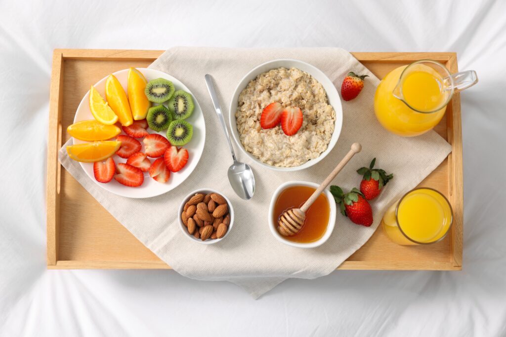 Tasty breakfast served in bed. Oatmeal, juice, fruits, almonds and honey on tray, top view