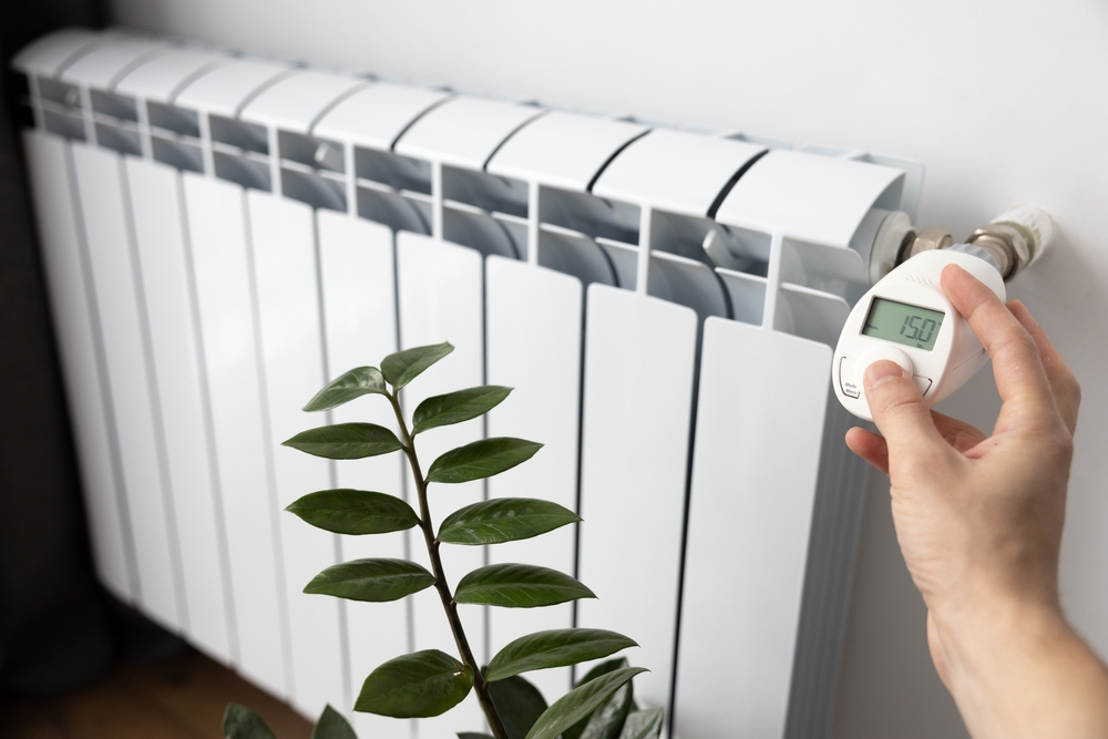 A person sets the heating temperature on an electronic thermostat with his hand. Stylish white heating battery in the house. Raises, lowers the room temperature. Heating technologies.
