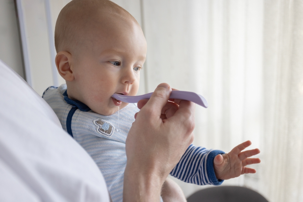 Father feeding his baby with yogurt at home. Feeding the baby in an upright position.