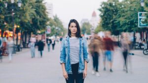 9 Traits of People Who Love To Be Alone, Backed By Science Woman on a city walk way. Image has a photographic effect known as a "time-lapse portrait" or "long-exposure," where a central subject remains perfectly still while the surrounding crowd is blurred by movement.