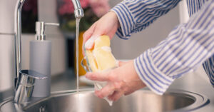 Ways Your Kitchen Sponge Could Be Slowly Killing You person using kitchen sponge in sink