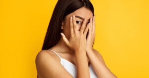 10+ Habits or Behaviors of a Very Insecure Person insecure woman hiding face with hands yellow background