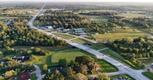 Morning aerial view of State Highway 646 in Santa Fe, Texas, captured from 184 feet. The road stretches towards Dickinson, surrounded by greenery under a peaceful sky.