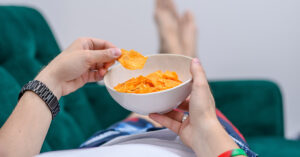 31 Foods You Should Avoid Eating, According to Experts person eating crisps on the sofa