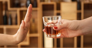 Man Shares Life-Changing Results Of Quitting Alcohol After 20 Years of Drinking person rejecting alcohol with hand placed in front of drink being offered. Sober, sobriety concept