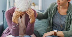elderly woman with face in palms of hand being comforted.