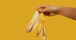 10+ Unexpected Ways to Use Banana Peels You Didn’t Know About person holding a banana peel ready to drop it. Yellow background