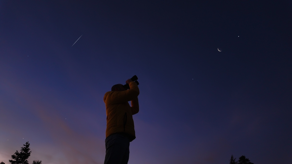 Amateur astronomer looking at the evening skies, observing planets, stars, Moon and other celestial objects with binoculars.
