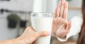 8 Signs You May Be Lactose Intolerant person putting their hand up in refusal to a glass of milk. Lactose intolerance concept