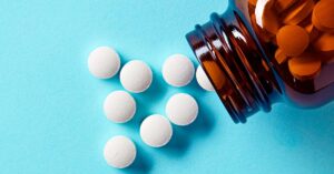 Popular Over-The-Counter Tablet Taken By Millions May Increase Dementia Risk brown glass jar with white pill spilling out on blue surface