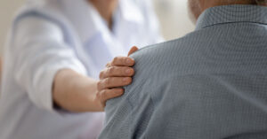 Close up caring doctor touching mature patient shoulder expressing empathy and support young woman therapist physician comforting senior aged man at meeting medical healthcare and help
