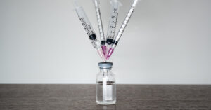 Iowa Moves Forward with Legislation to Prohibit mRNA Vaccines multiple syringes stuck into vile. Vaccine concept