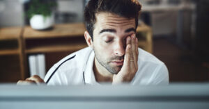 Experiencing Burnout? Here’s One Early Sign to Watch For exhausted man wiping his eyes from burn out. sympyoms of burnout concpet