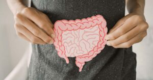 person with small and large intestine illustrated on a piece of paper holding over their abdomen. Gut health concept