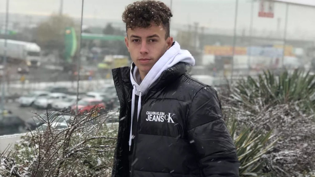 19-year-old Luca Manolache in a black jacket stands in the snow, surrounded by bushes, capturing a winter moment.