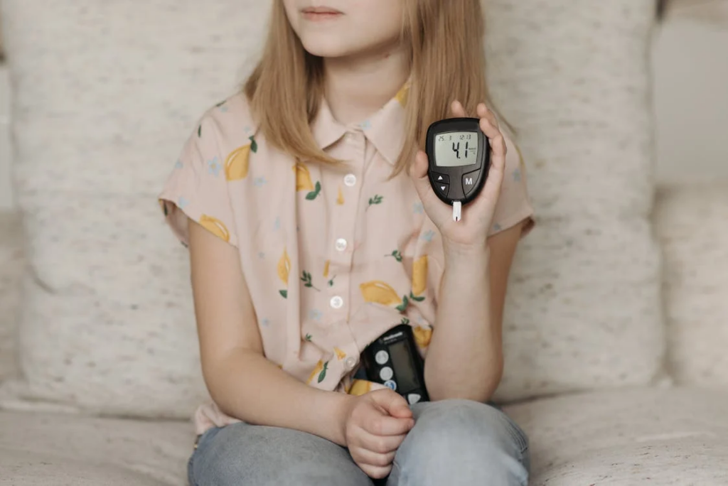 Little Girl Sitting on the Sofa and Showing Her Glucometer