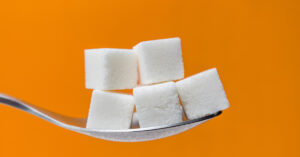 6 Things That Could Happen When You Stop Eating Sugar 5 sugar cubes on a teaspoon with orange background