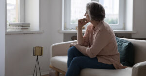 elderly woman sitting on couch looking concerned while looking out a window