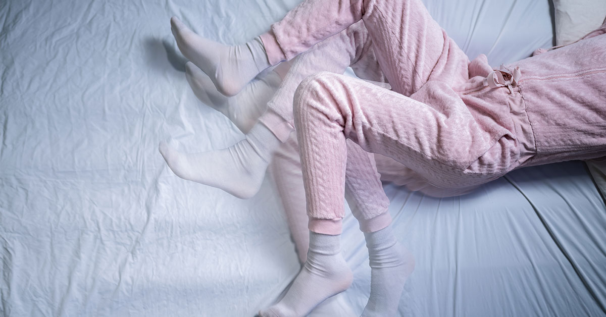 woman in pink laying bed with legs moving rapidly; Restless leg syndrome concept