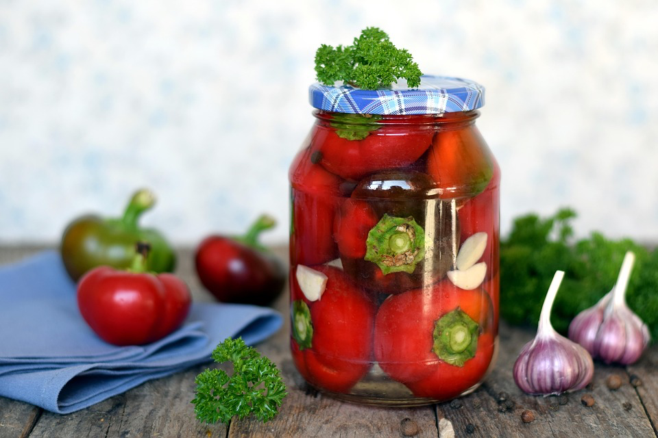 Preserved red vegetables in a glass jar with fresh herbs and garlic cloves, showcasing the traditional food preservation methods that provide flavorful alternatives to commercially processed products.