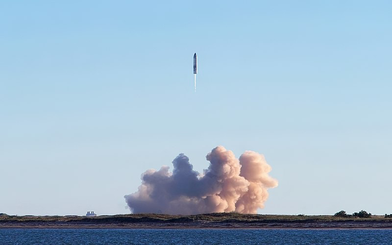 A SpaceX Starship rocket takes off from the launchpad. Thick smoke rises as it begins its flight. This launch led to a Starship explosion later in the test.