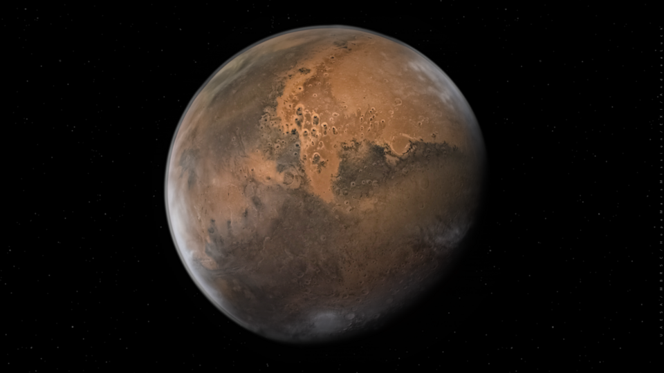 High-resolution photograph of Mars showing its distinctive reddish-orange surface with visible dark regions and polar ice caps against the black background of space. The planet's atmosphere appears as a thin bluish haze around its curved edge.