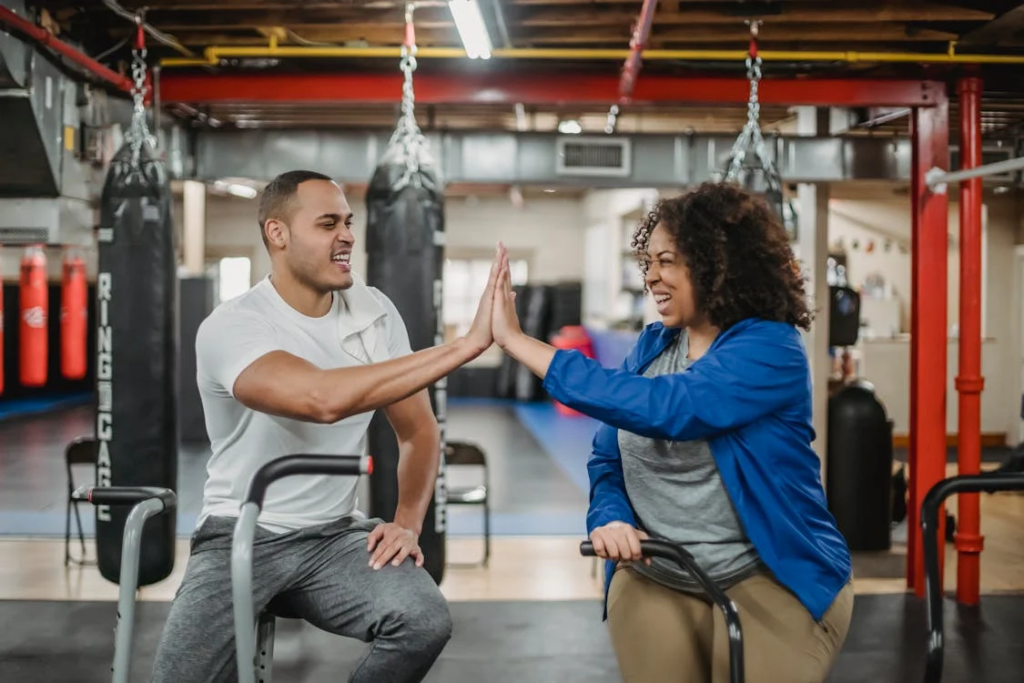 Excited diverse trainee and fitness instructor clapping hands in gym