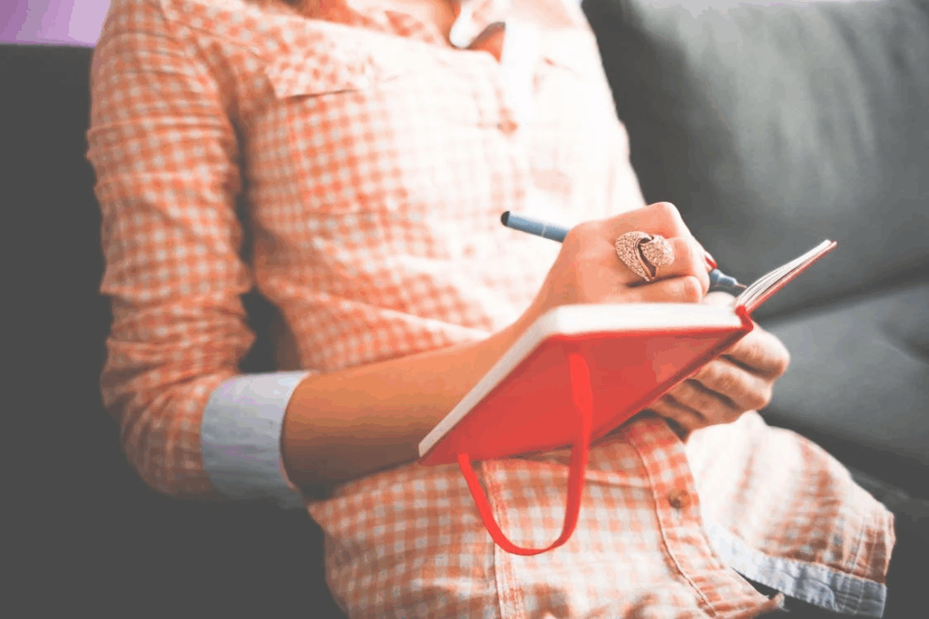 Person Writing on Red Notebook