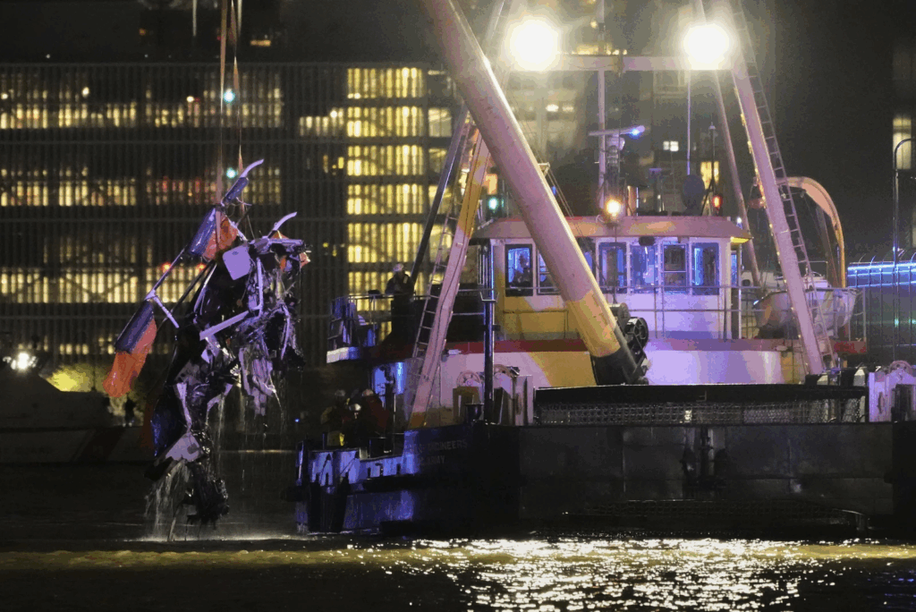 Large crain removing the reckage of the helicopter from the water at night time.