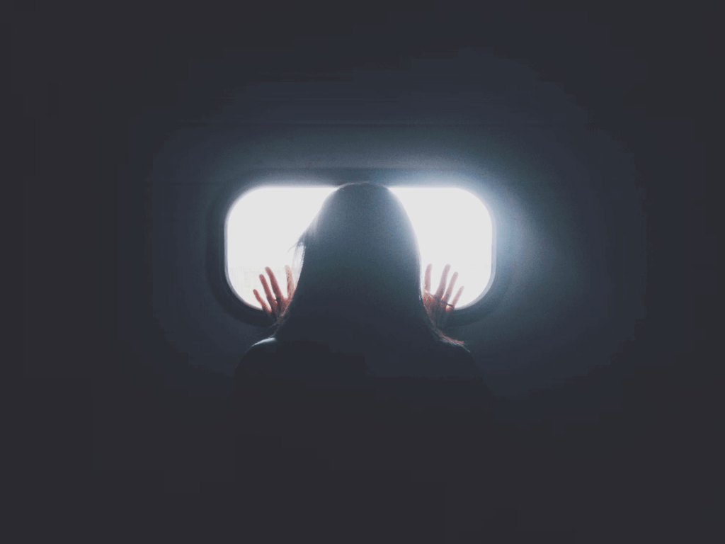 Silhouette of a person with hands pressed against a bright rectangular window in darkness, symbolizing consciousness trapped at the threshold between life and death during the minutes when the brain remains active after clinical death is declared.