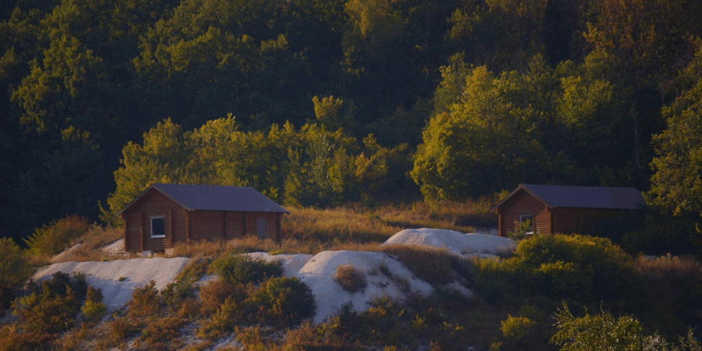 Two wooden eco-resort cabins nestled in a Swedish forest landscape, representing the type of sustainable tourism accommodation that was promised at Stedsans. This eco-resort marketing image contrasts with the environmental reality discovered after the owners abandoned the property.