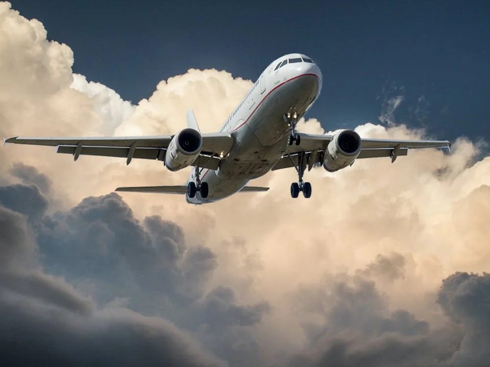 Commercial passenger airplane taking off through dramatic clouds against a blue sky background.