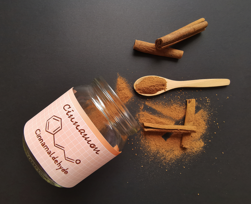 Cinnamon sticks and milled cinnamon spice in the glass jar with structural chemical formula of cinnamaldehyde (the major component of cinnamon). Winter spices, cinnamon sticks with spoonful of powder.