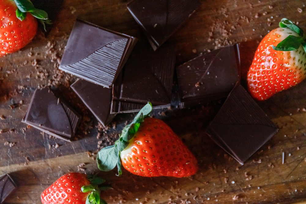 Strawberries and chocolate on a wooden cutting board. Fresh berries with pieces of dark chocolate, ingredients for a birthday cake.