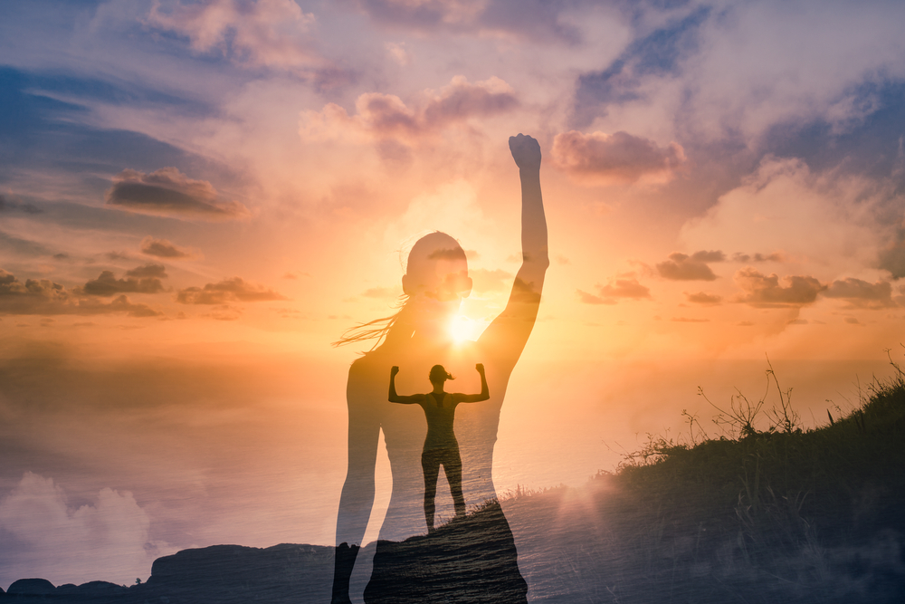 Strong successful woman on a mountain flexing arms feeling inspired, and motivated.
