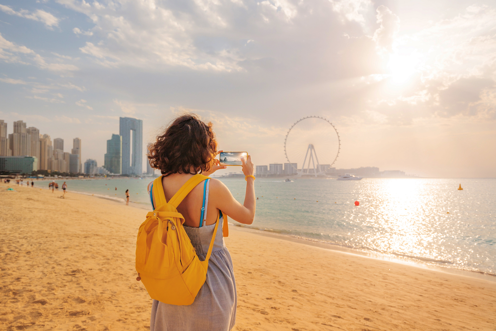 Woman travel blogger takes pictures for social networks of skyscrapers on Bluewaters island and the famous Ain Ferris Wheel in Dubai
