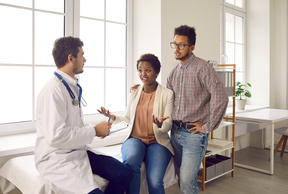 Multiethnic couple consult with male gynecologist about pregnancy planning. Ethnic international spouses have consultation with family doctor about fertility treatment. Healthcare concept.
