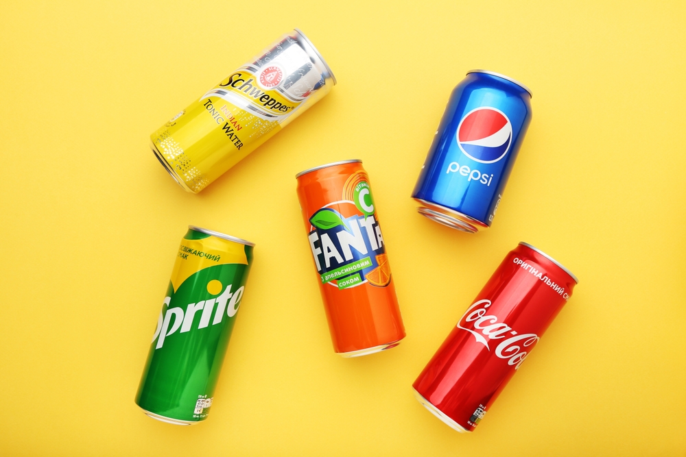 MYKOLAIV, UKRAINE - JANUARY 15, 2021: Cans of Coca-Cola, Pepsi, Fanta, Sprite and Schweppes drink on yellow background

