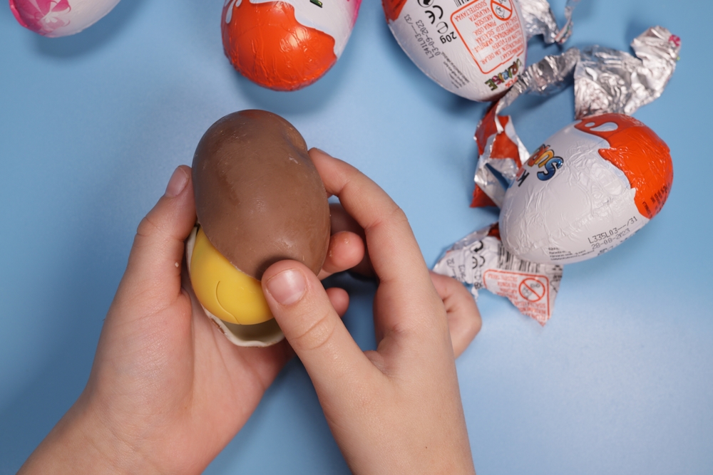 Magdalinovka, Ukraine - March 3, 2023. Child opens Kinder Surprise on a blue background