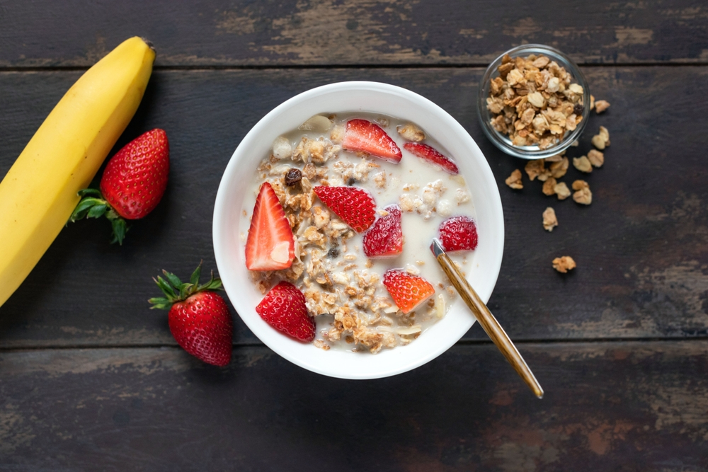 Granola bowl with strawberries and oat milk on a wooden table background, top view. Healthy breakfast meal