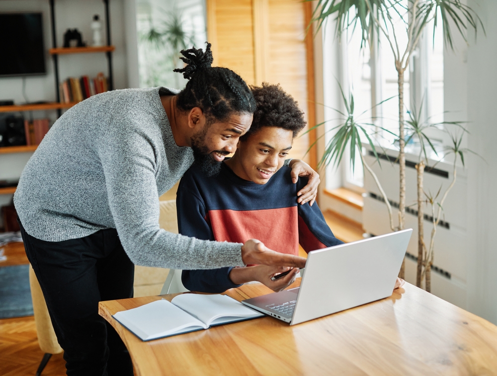 Father and son doing homework with laptop at home. Father and teenage son using laptop. Boy and dad sitting at home working with notebook