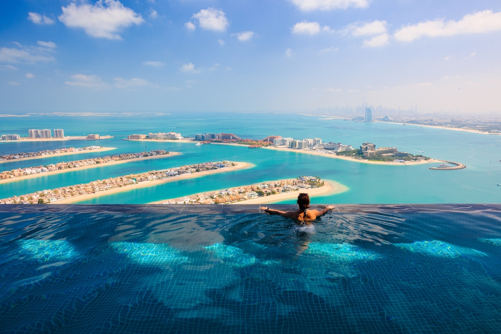 Young woman in luxury infinity pool over Palm Jumeirah islands and Dubai Marina city skyline