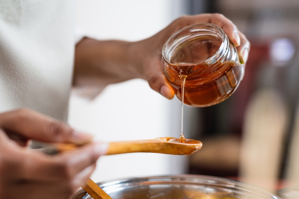 Female hands holding a bowl of bee honey and a wooden spoon. Close up. Elaboration of organic soap based on glycerin.