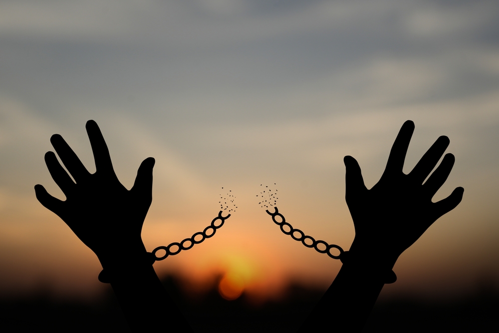 Freedom concept. The shadow of a pigeon is released from the chains that bind human arms. golden sun background in the morning
