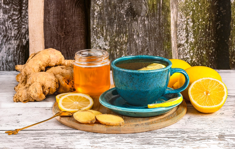 Two blue cups and ingredients for ginger tea, honey, lemons, ginger root on wooden background, side view