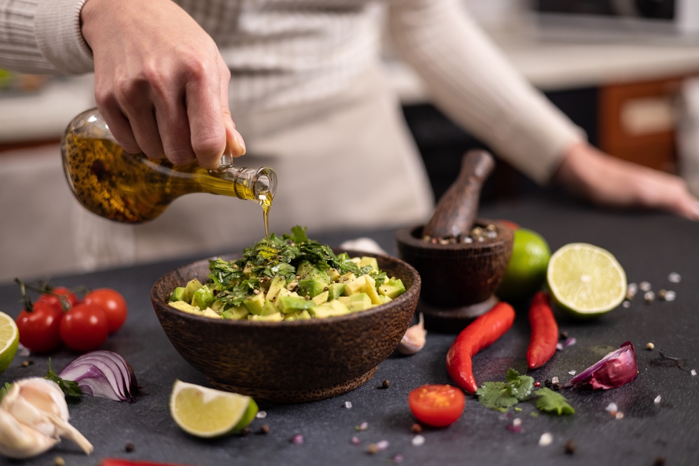 Cooking traditional salsa - woman pours olive oil into bowl with sliced chopped ingredients