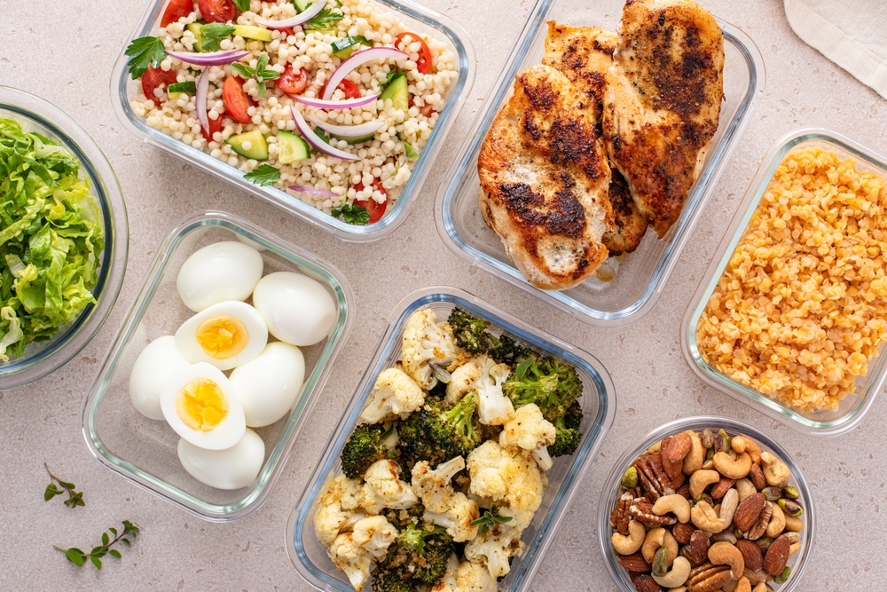 Healthy high protein meal prep with cooked chicken breast, boiled eggs, roasted vegetables, cooked lentils, couscous salad and mixed nuts