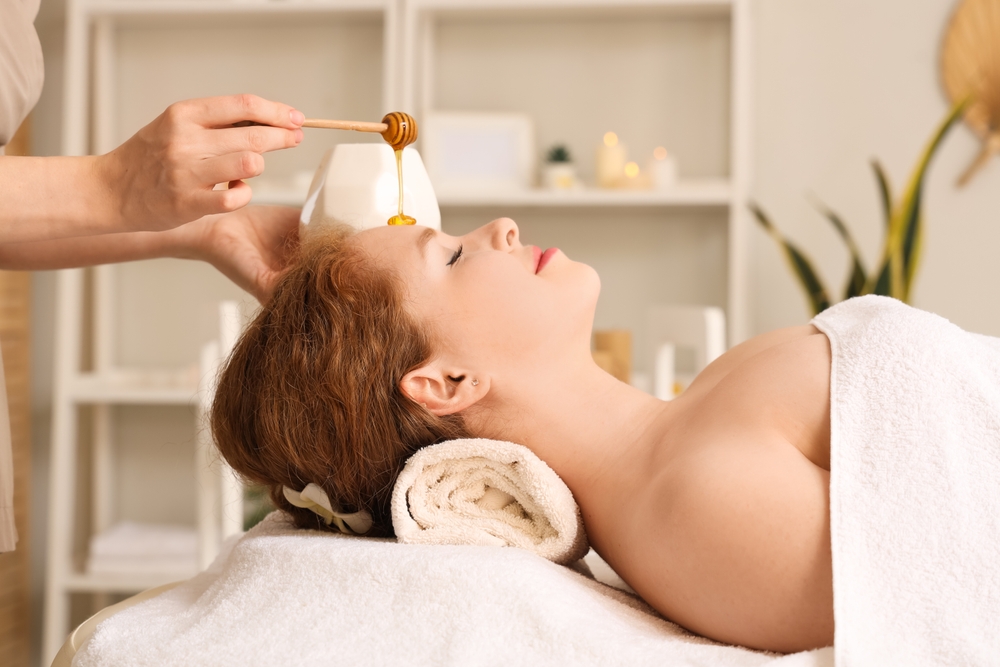 Massage therapist pouring honey on woman's face in spa salon, closeup