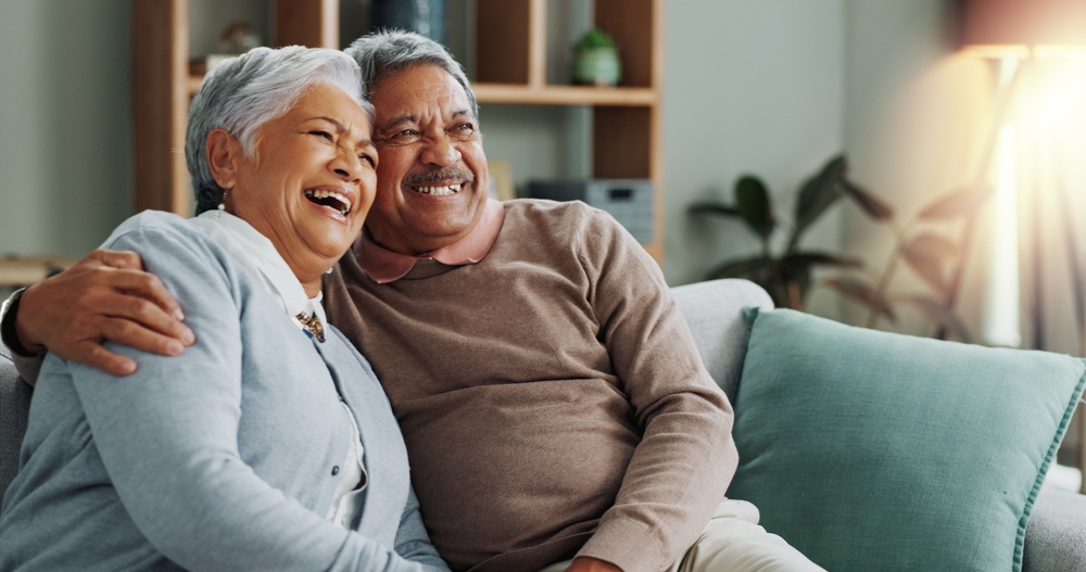 Senior, couple and hugging on sofa in home together, elderly apartment and care with married people for love. Relationship, commitment and pensioners in retirement relax on couch for bonding