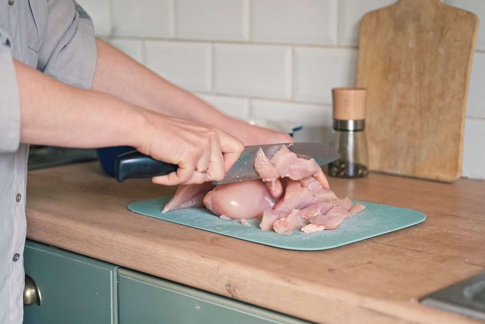 Female butcher cut raw meat with sharp knife at home kitchen. Woman cutting the chicken fillet in pieces for cooking. Preparing chopping food. Split poultry breast. Healthy lean meat, low cholesterol